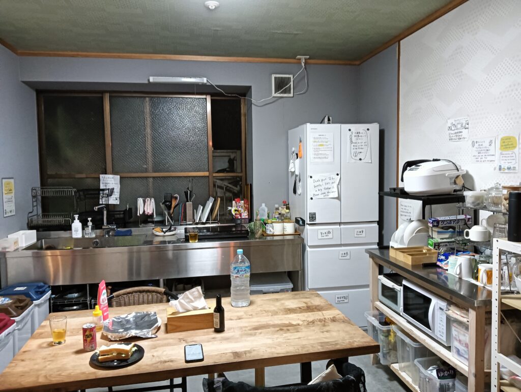ゲストハウスの共有キッチン。流し台や冷蔵庫、木のテーブルなどが並び、落ち着いた共同スペースになっている。